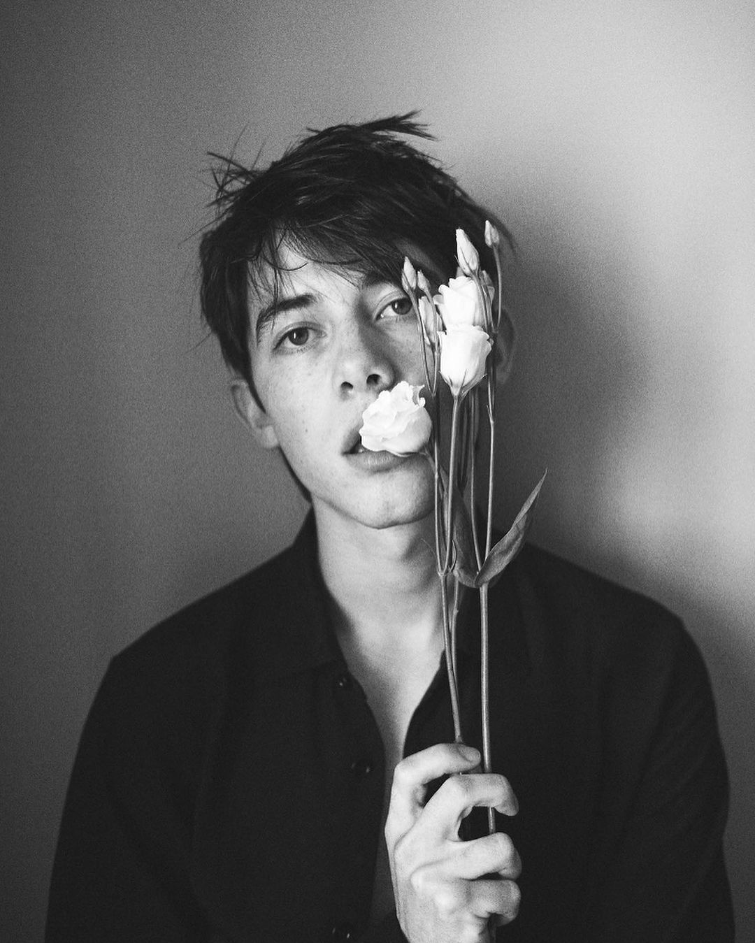 Black and white portrait of a young adult holding a bouquet of lisianthus flowers with one flower held in their mouth.
