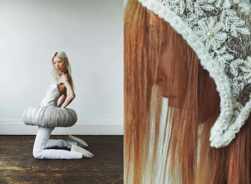 Woman in modern outfit kneeling indoors with blonde hair, wearing a white dress with textured leggings and ballet flats on a wood floor.