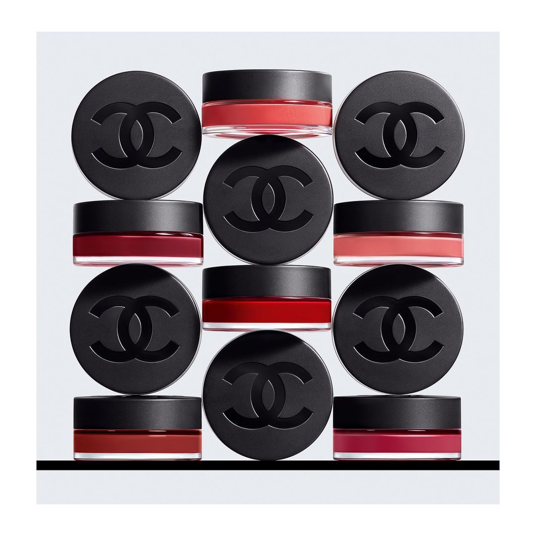 Nine jars of Chanel makeup are displayed against a grey background in an evenly spaced arrangement creating a visually appealing pattern.