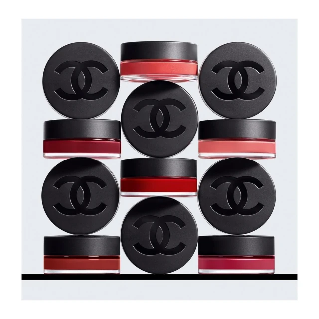 Nine jars of Chanel makeup are displayed against a grey background in an evenly spaced arrangement creating a visually appealing pattern.