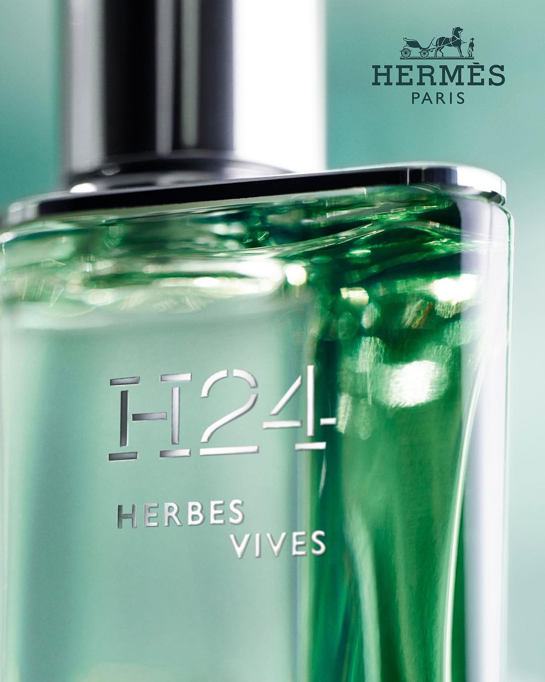 Close-up of a clear glass perfume bottle with a silver cap, featuring the Hermès logo and the words 'H24 Herbes Vives' in silver text.