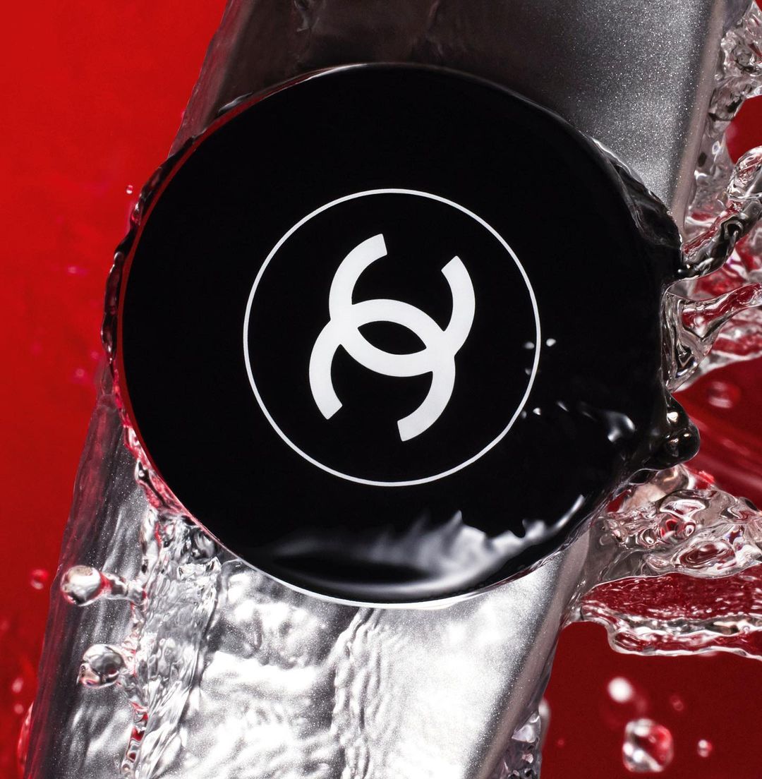 Chanel logo on a bottle with water droplets against a red background, showcasing a beauty product in a dynamic studio shot.