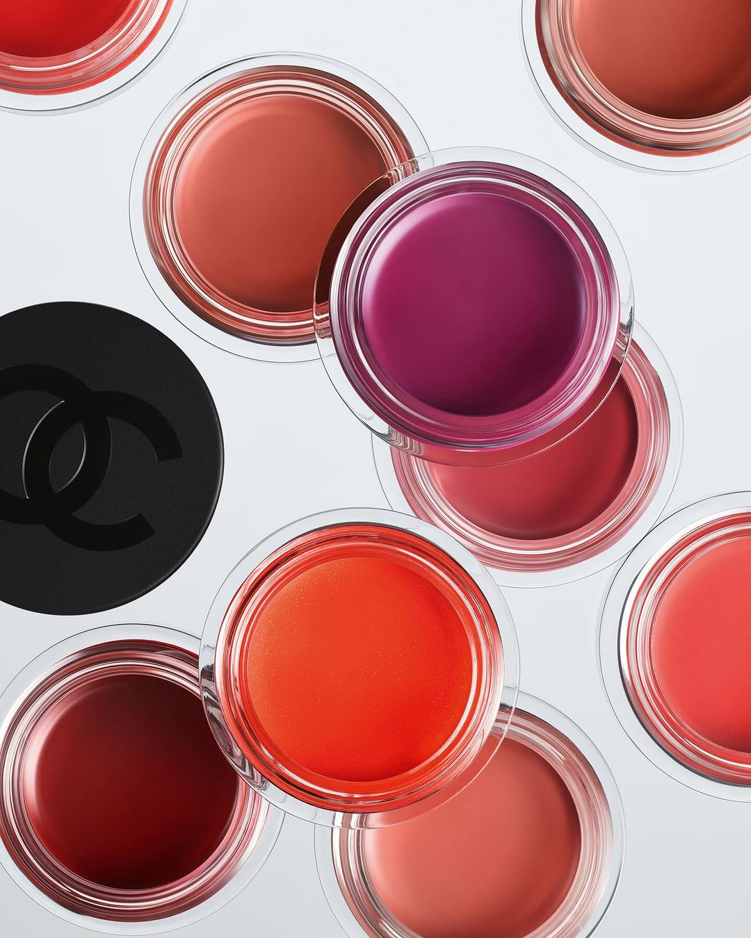 Overhead shot of assorted Chanel lipsticks in clear jars, arranged on a bright white surface, with the Chanel logo visible.