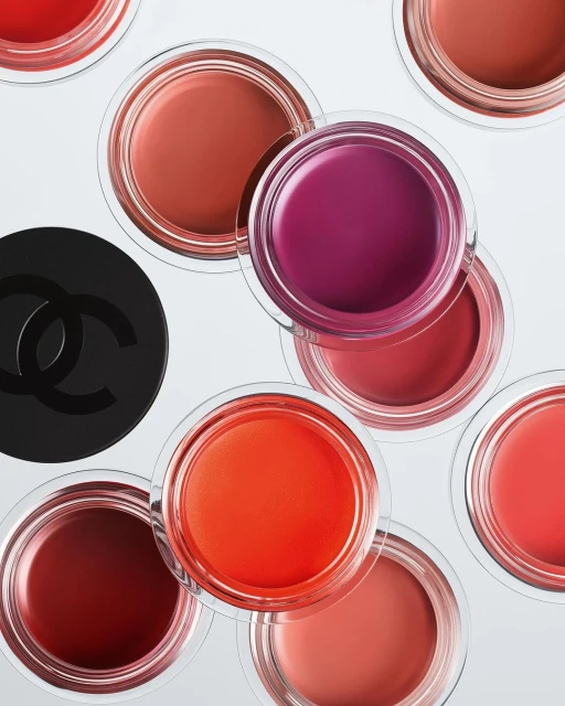 Overhead shot of assorted Chanel lipsticks in clear jars, arranged on a bright white surface, with the Chanel logo visible.