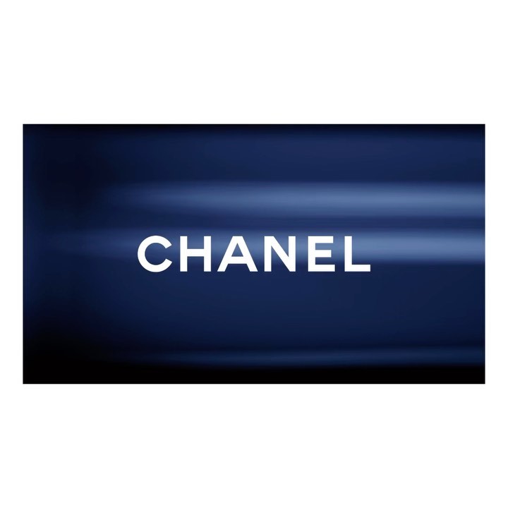 Bright white "CHANEL" text against a dark blue, softly blurred background in a horizontal product shot, ideal for beauty advertising.