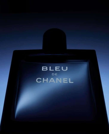 Chanel Bleu perfume bottle with dramatic lighting on a dark blue gradient background, showcasing its elegant design and appeal.