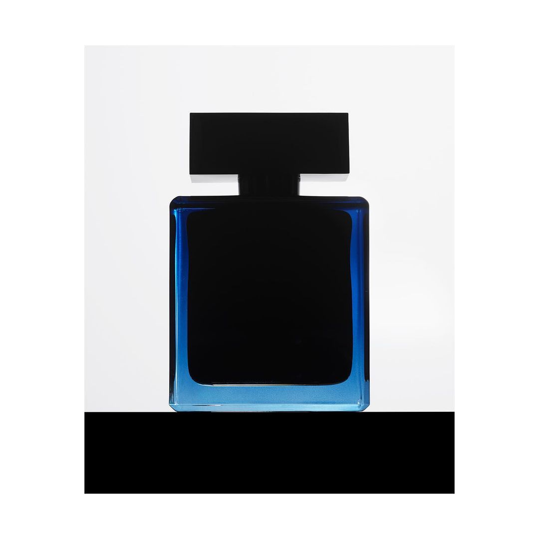 Elegant, squared perfume bottle featuring dark liquid enclosed by a transparent blue glass frame, set against a clean, white backdrop.