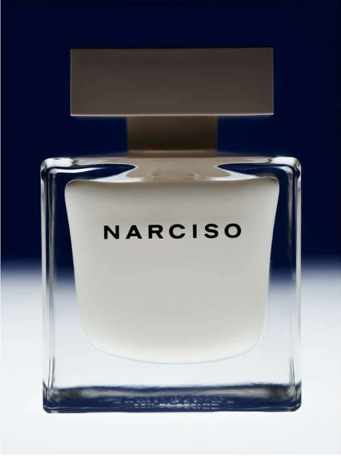 Narciso Rodriguez perfume bottle in clear glass with a white block, shot in studio with a dark gradient blue background.