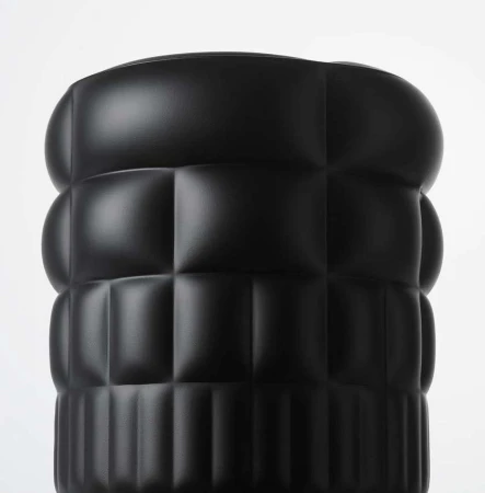 Close-up of a black textured cylinder with rounded edges and a grid pattern against a plain white background, showcasing modern design.