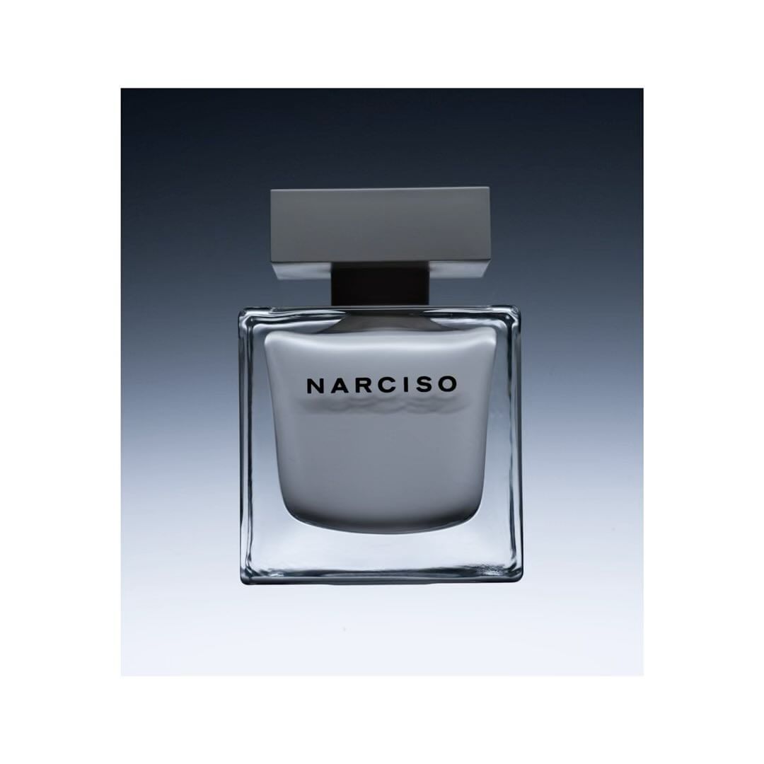 Close-up studio shot of a square glass Narciso Rodriguez perfume bottle with a gray cap, against a gradient gray background.