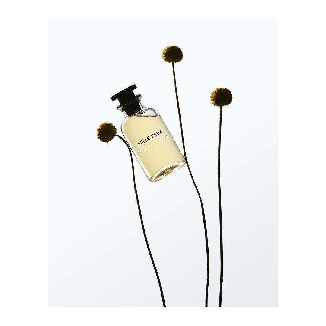 Perfume bottle of Mille Feux by Louis Vuitton stands out against a soft white background with floral accents, embodying elegance and simplicity.