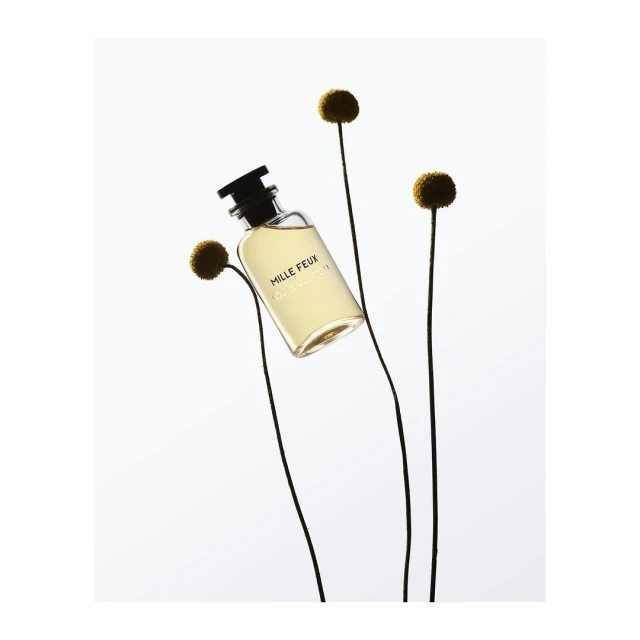 Perfume bottle of Mille Feux by Louis Vuitton stands out against a soft white background with floral accents, embodying elegance and simplicity.