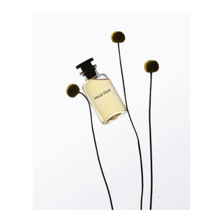Perfume bottle of Mille Feux by Louis Vuitton stands out against a soft white background with floral accents, embodying elegance and simplicity.