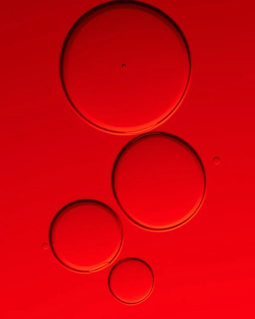 Abstract still life featuring four translucent spheres in varying sizes against a vibrant red background with subtle light and shadow play.