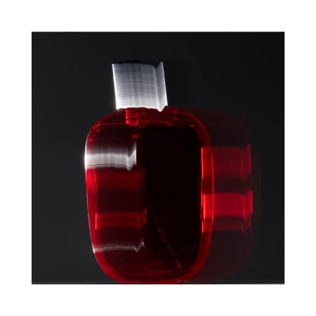 A glossy red glass perfume bottle with a silver cap sits against a dark background, showcasing motion blur and light painting effects.