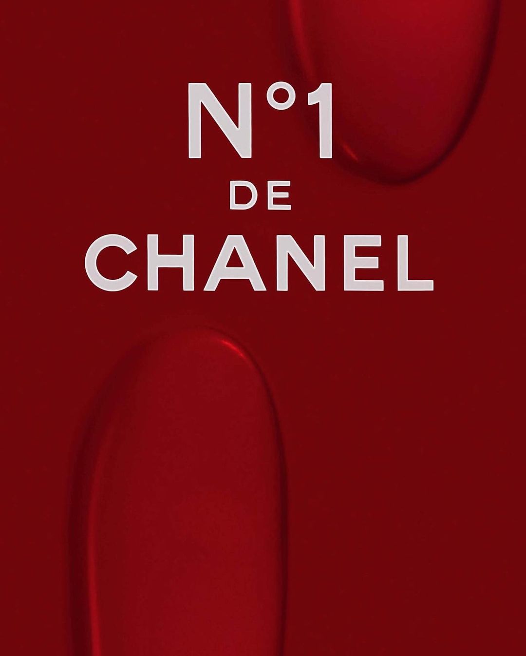 Close-up of Chanel No. 1 beauty product advertisement featuring product name and brand logo on a red gradient background.