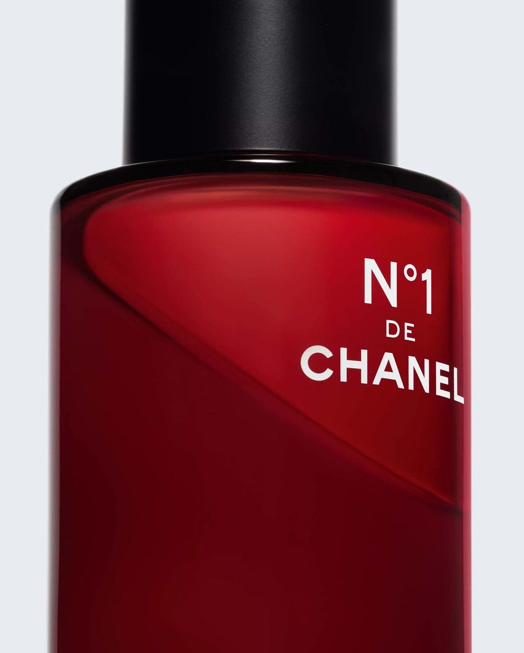 Close-up studio shot of a red Chanel N°1 de Chanel bottle with a black cap and white logo, set against a neutral background.