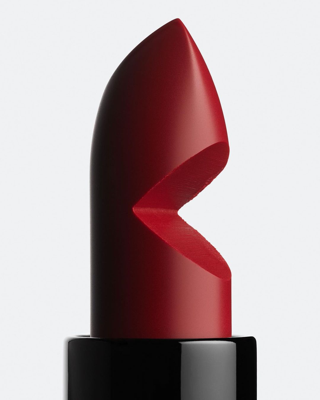Close-up of a red lipstick bullet with a carved design on a black tube against a white background, product photography, beauty.
