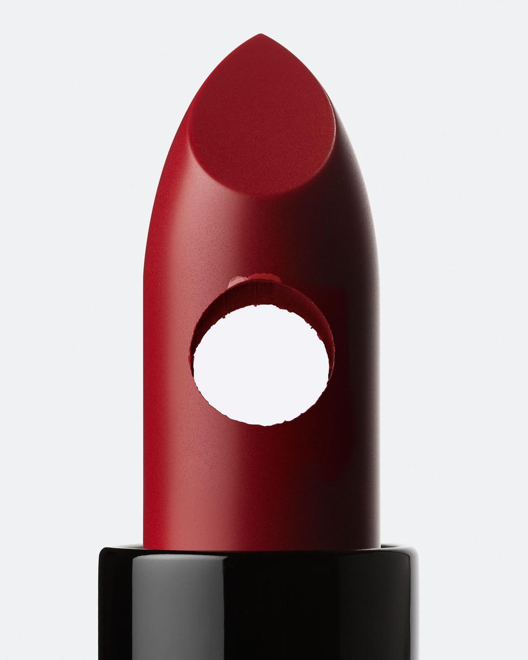 Close-up of a red lipstick with a circular hole in the middle, showcasing beauty product innovation on a solid white background.