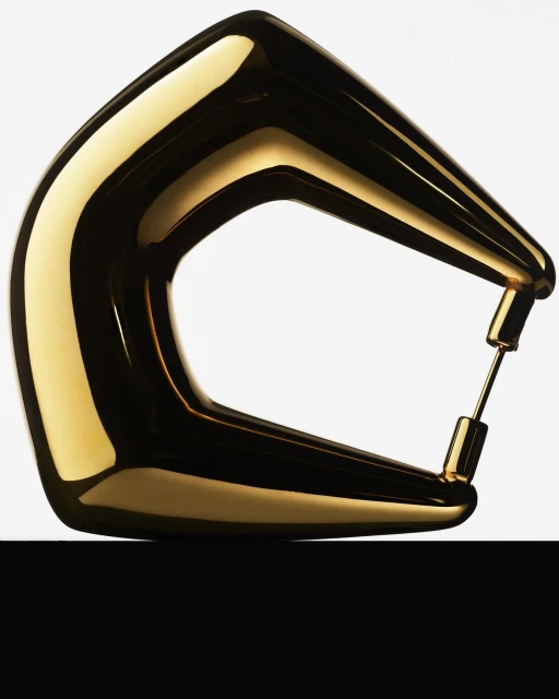 Close-up studio shot of a gold-colored abstract metal sculpture with sleek, rounded shapes against a white background and black base.