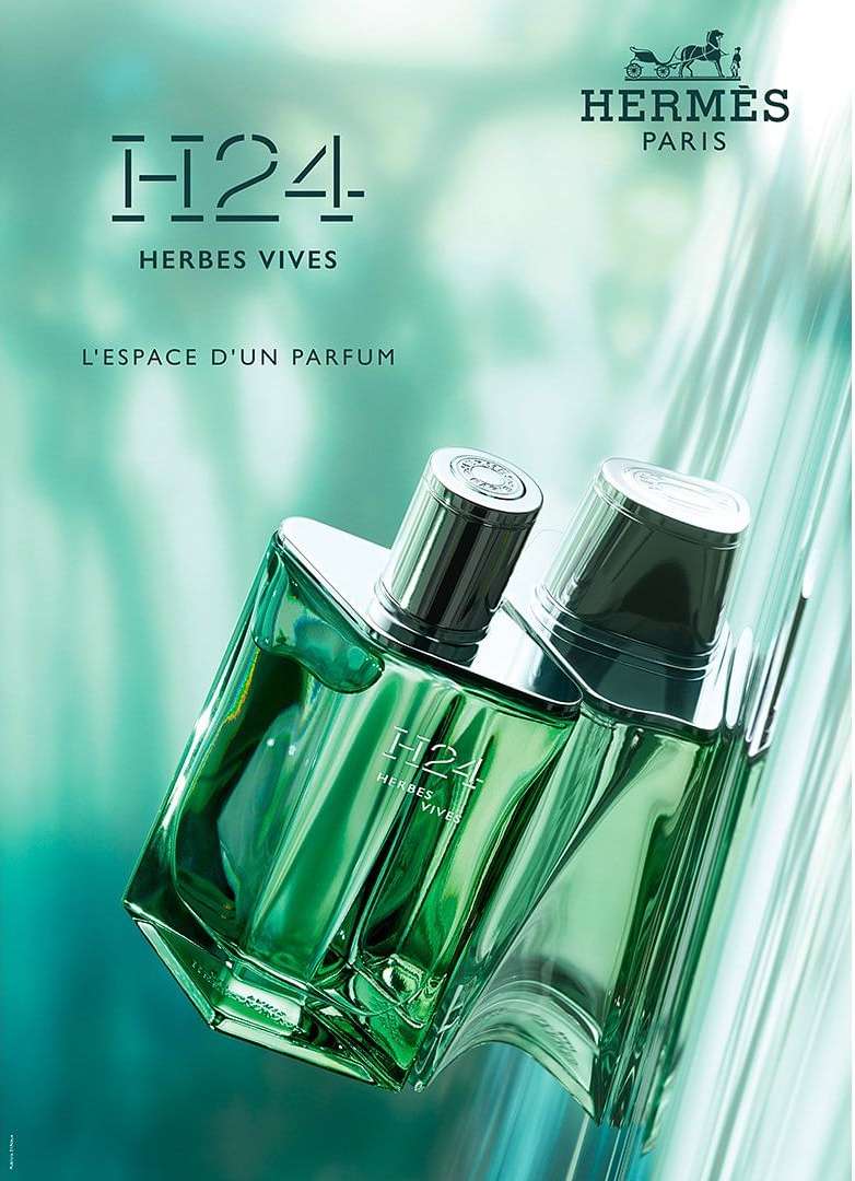 Hermes H24 Herbes Vives fragrance: Two perfume bottles, transparent green glass, silver caps, close-up on a turquoise background.