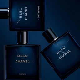 Three dark blue rectangular fragrance bottles arranged diagonally against a deep navy blue background with dramatic lighting.