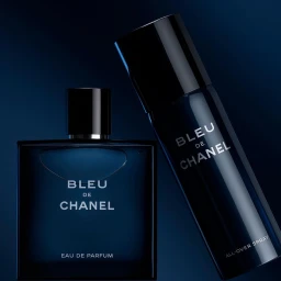 Bleu de Chanel eau de parfum bottle and all-over spray bottle against a dark blue background with studio lighting