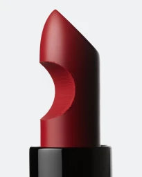 Extreme close up of a dark red matte lipstick in a black tube with a circular cutout chunk removed from the side against a white background.