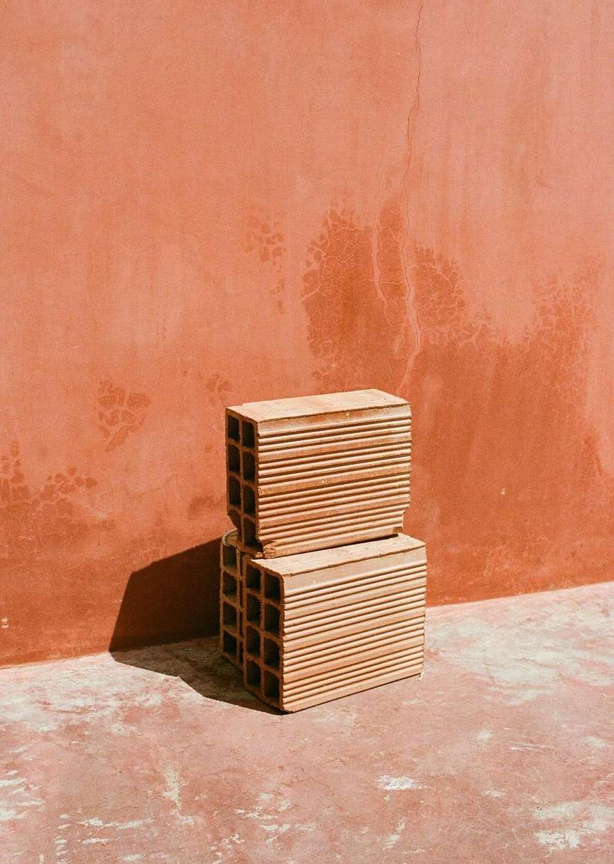 Stacked terracotta blocks against a terracotta wall, creating a minimalist architectural still life with a warm, earthy color palette.