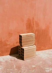Two terracotta hollow bricks stacked on a weathered reddish-orange ground against a textured matching wall.