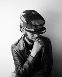 Portrait of a man wearing a patchwork flat cap and leather jacket, photographed by Ollie Trenchard in London.