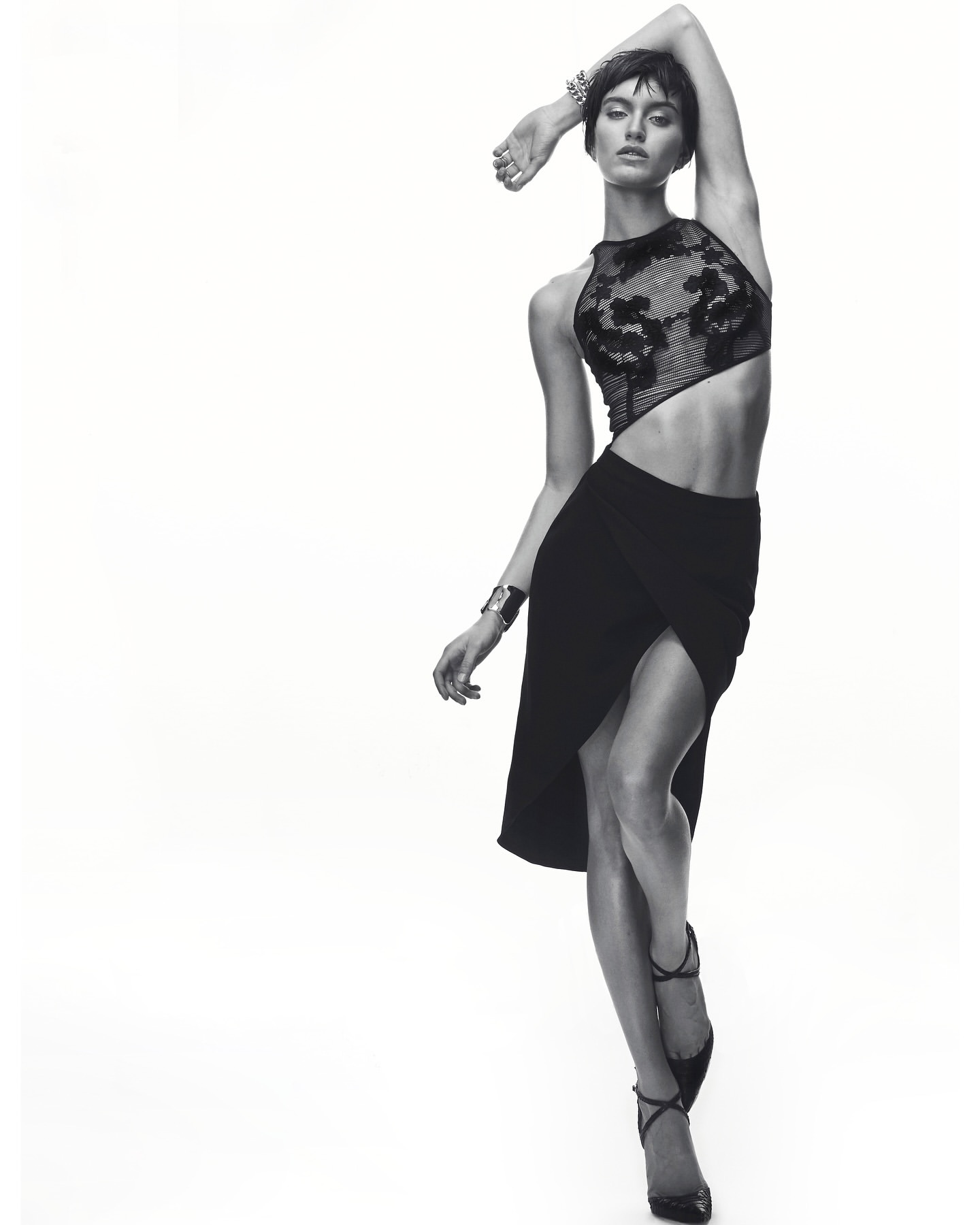 Black and white fashion shot of a slim woman in a stylish black top and skirt, posing against a white backdrop with soft lighting.