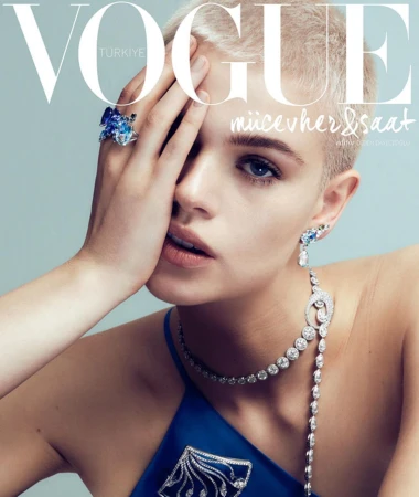Close-up portrait of a blonde model wearing a blue top, ornate diamond necklace, and large gemstone ring, photographed by Onur Dag.