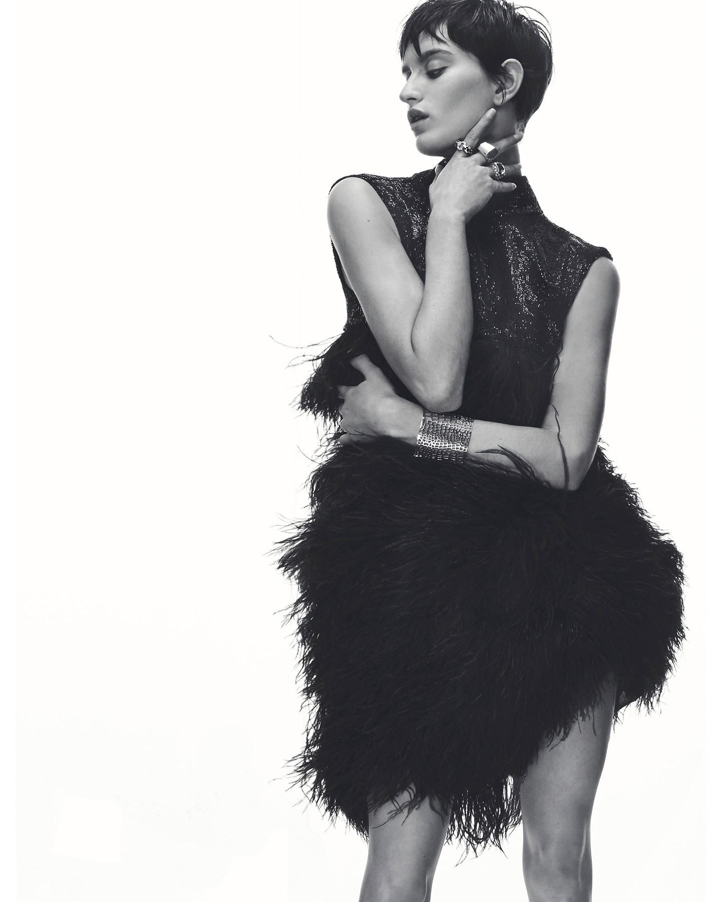 Monochrome portrait of a stylish adult woman with short dark hair in a sleeveless black dress posing against a bright white backdrop.