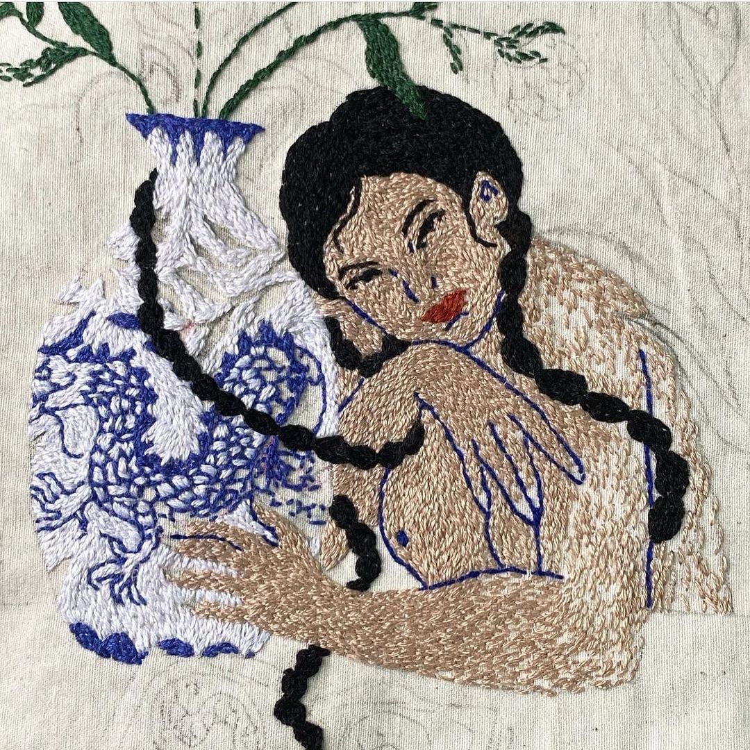 Embroidered image features a woman embracing a vase; black braided hair, red lips. Textile art with blue and white porcelain vase.
