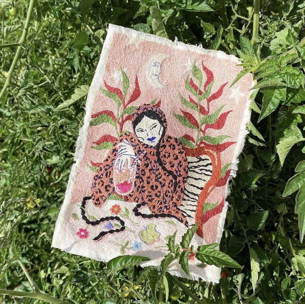 Illustration on fabric featuring a woman in a leopard-print outfit holding a pink drink, surrounded by plants in a garden setting.