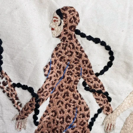 Close-up of fabric embroidery featuring a stylized figure in a leopard print bodysuit against an off-white background