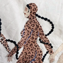 Close-up of fabric embroidery featuring a stylized figure in a leopard print bodysuit against an off-white background