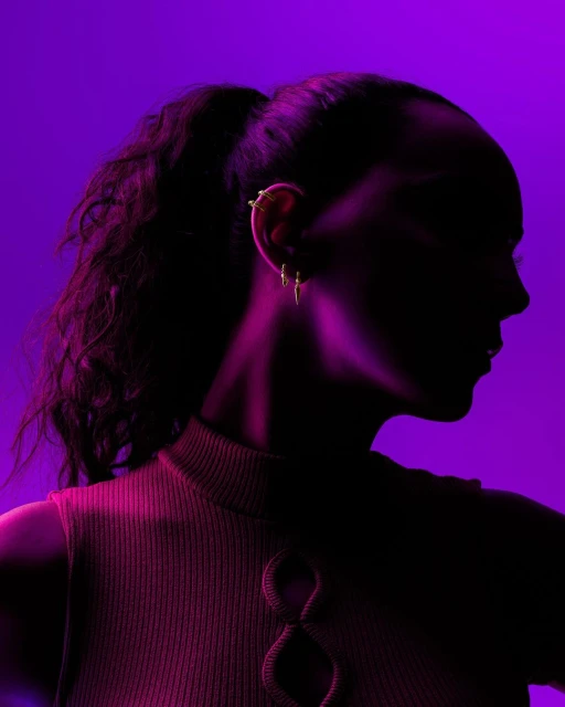 Profile view of a woman with an ear cuff and three earrings, wearing a mauve shirt, against a vibrant purple background.
