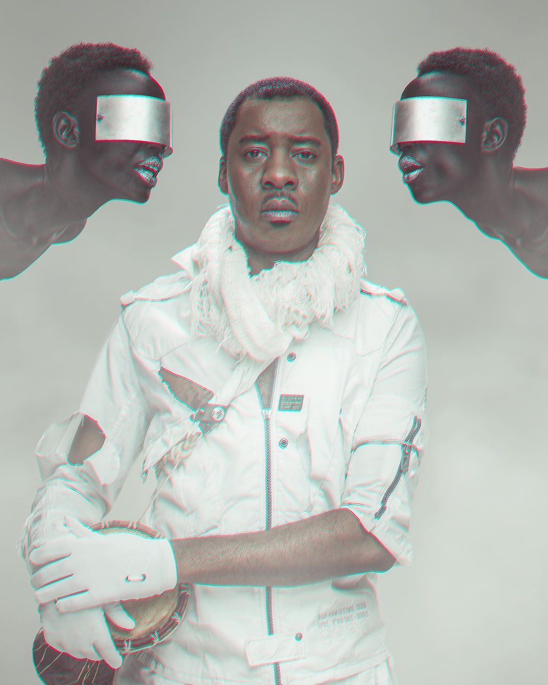Studio portrait of a man in a white jacket holding a drum, flanked by two figures with mirrored visors against a soft grey backdrop.