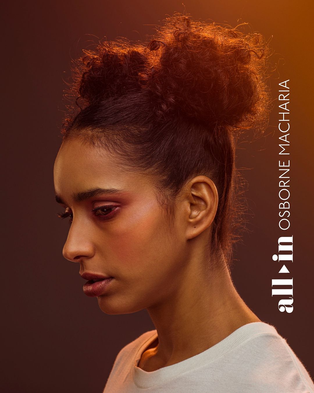 Portrait of a young African-American woman with a thoughtful expression, styled with an updo hairstyle and wearing a white top, against a gradient orange background.