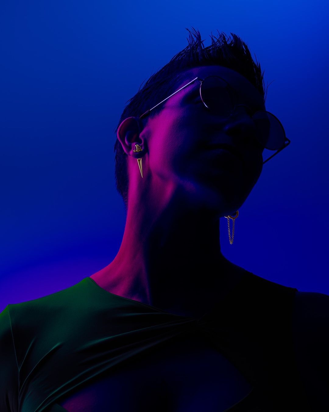 Silhouette of a stylish adult with an undercut and geometric gold earrings, wearing sunglasses against a vibrant blue backdrop.