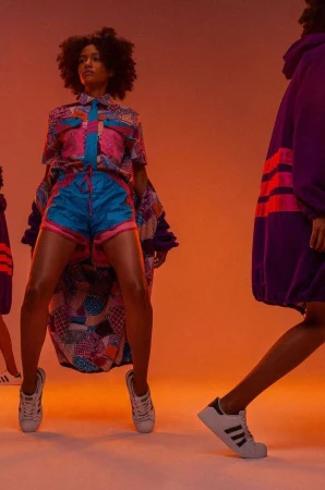 Two women in colorful, patterned outfits pose in a photo studio with vibrant orange lighting, showcasing fashion and sportswear styles.