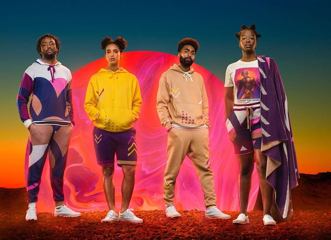 Four adult fashion models in casual streetwear pose in front of a surreal red planet and horizon on a textured reddish-brown terrain.