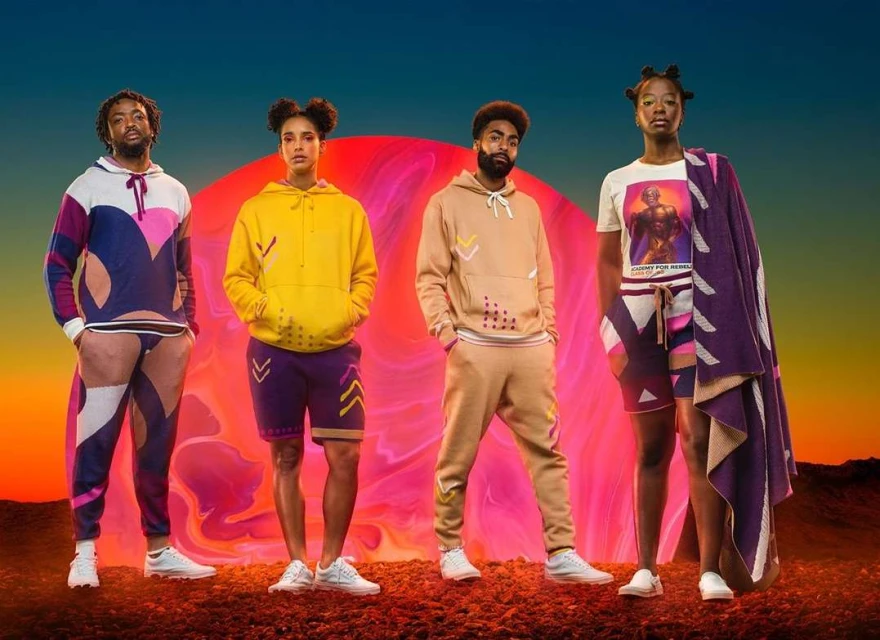 Four adult fashion models in casual streetwear pose in front of a surreal red planet and horizon on a textured reddish-brown terrain.
