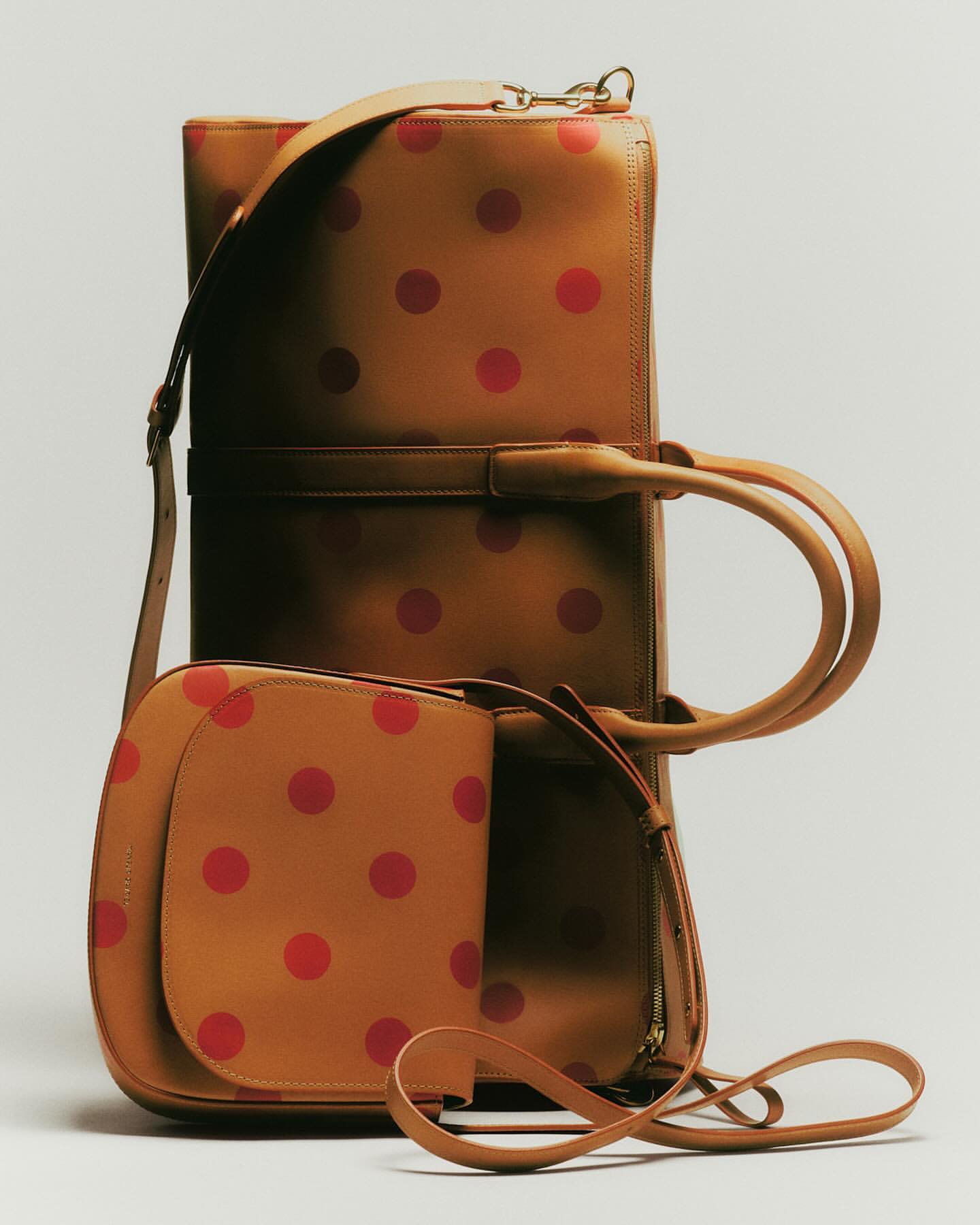 Tan leather luggage set with red polka dot pattern, including large suitcase with handle and shoulder bag, studio shot, neutral background.