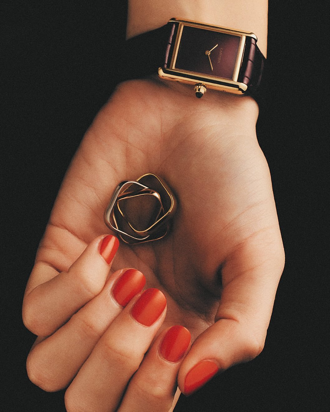 Overhead studio shot of an adult female's hand with red nail polish holding a rose-shaped silver object. Wristwatch is on her arm.