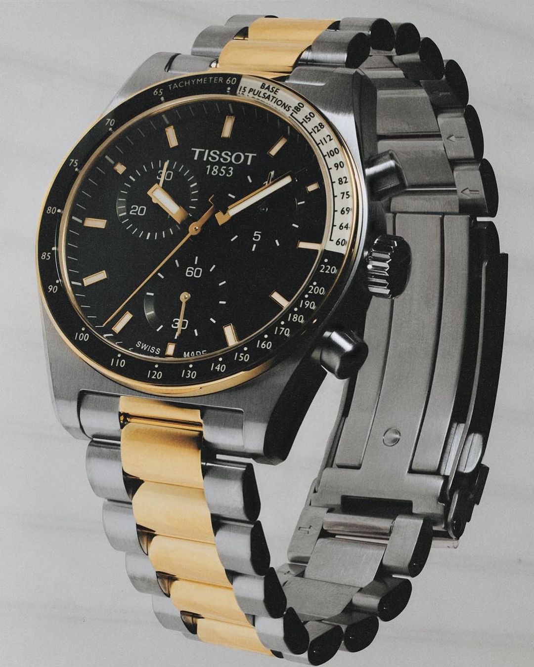 Close-up shot of a two-tone Tissot 1853 watch with a black dial and a stainless steel and gold bracelet.