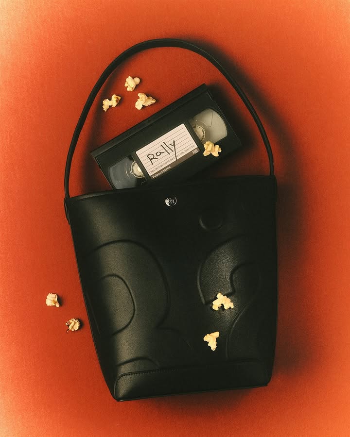 Black leather purse containing a VHS tape and popcorn on an orange backdrop for a vintage movie night concept.