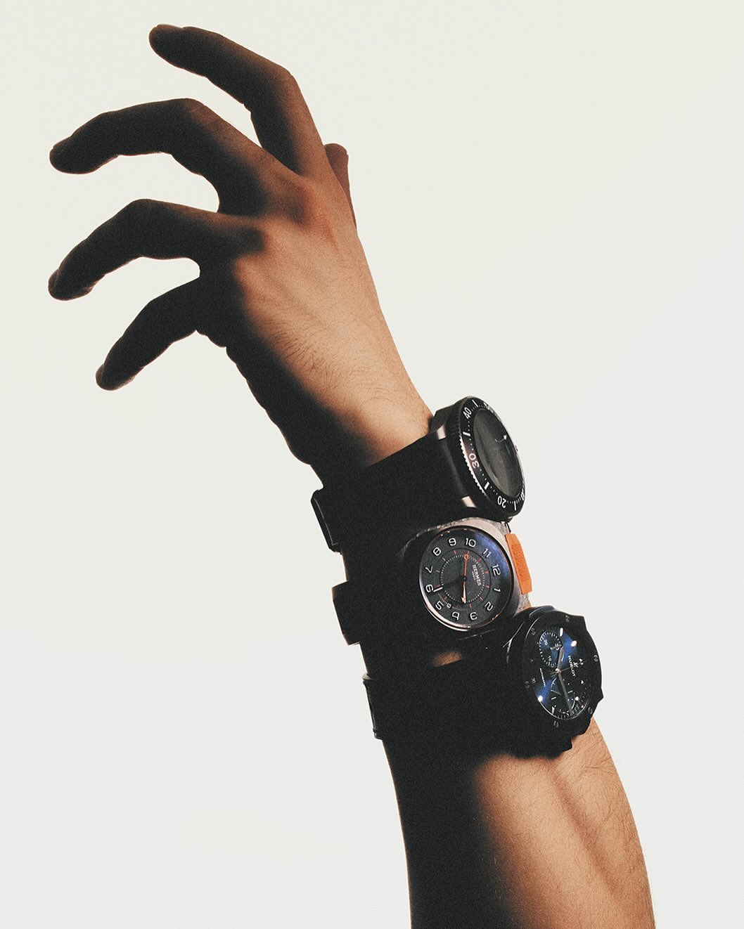 Close-up studio shot of an arm adorned with three wristwatches, showcasing a modern and fashionable aesthetic on a neutral background.